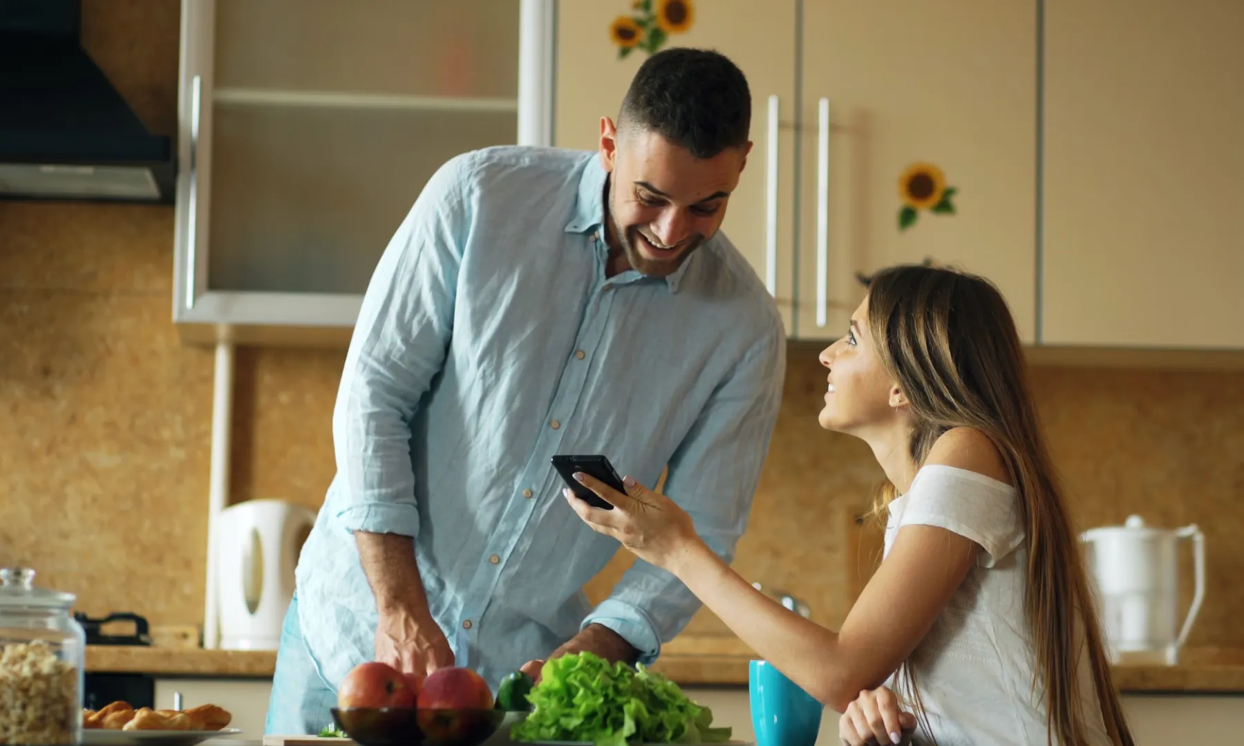 A young couple in their kitchen, smiling at a phone